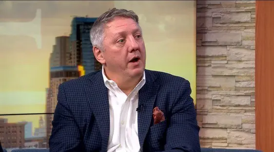 Man in blue suit speaks in studio.